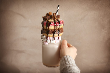 Hand holding milkshake, donuts and other sweets in jar on color background