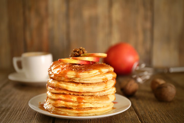 Delicious pancakes with maple syrup and sliced apple on wooden table