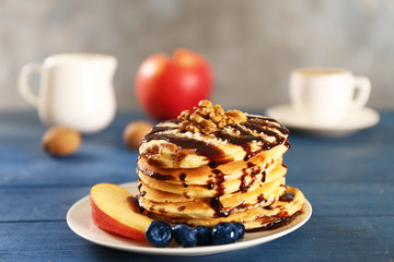 Delicious pancakes with chocolate syrup, blueberry and sliced apple on blue wooden table