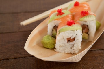 Four uramaki sushi served with chopsticks in wooden boat plate