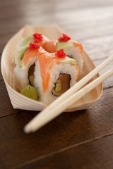 Four uramaki sushi served with chopsticks in wooden boat plate