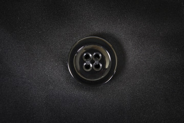 Black plastic button is sewn on black fabric