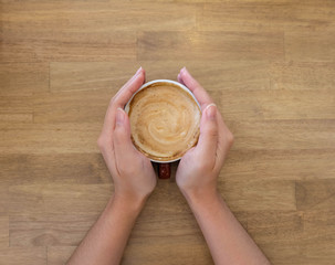 Woman hands holding a cup of coffee with latte art in a brown cu