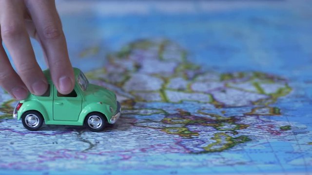 Human hand moving car model on world map, trip around Europe, vacation abroad