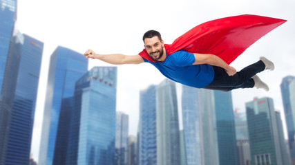 happy man in red superhero cape flying over city