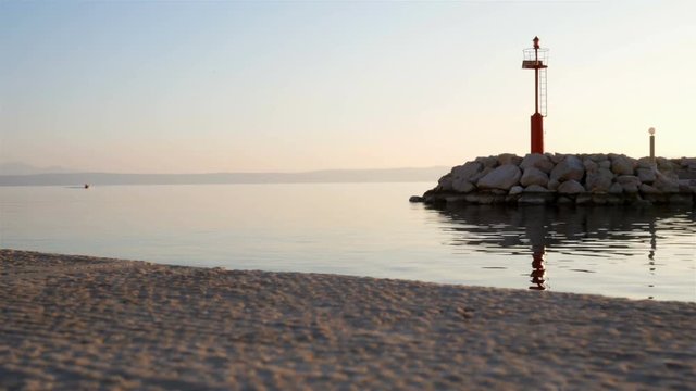 Calm sea at sunset on harbor entrance with marine light and small boat coming at background