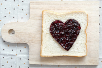 Toast with jam in shape of hearts on tablecloth background.  Top view