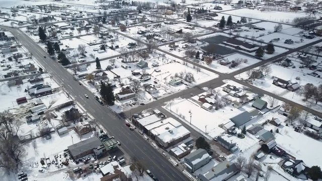 Aerial rural town center home business and traffic winter. Winter storm blizzard white snow. Rural farm community. Hard seasonal weather. Hazard to driving. Surveillance spy.