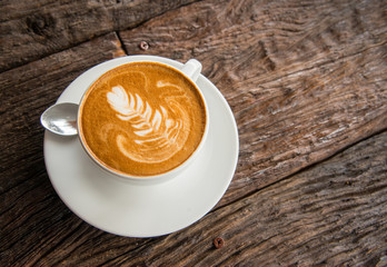 A cup of hot coffee with latte art on the surface placed in the wooden table.