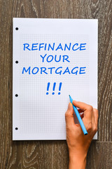 Woman hand writing refinance your mortgage on math book with marker