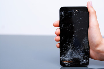 Close-up of broken mobile phone with cracked display in woman hand