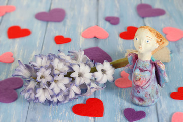 Ceramic clay angel near hyacinth flower and hearts on shabby blue wooden planks in rustic style.