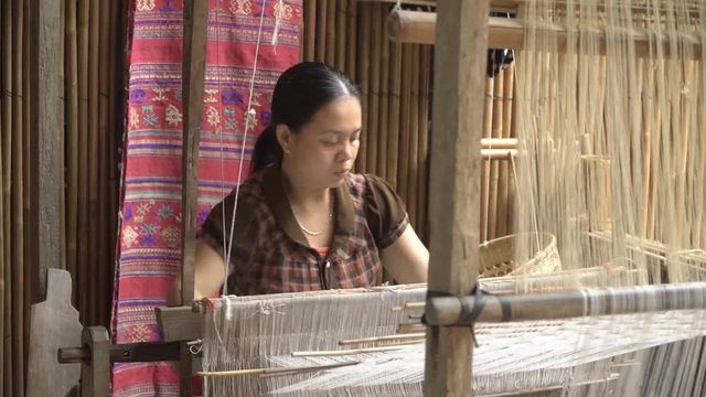 Woman working with a waist loom to finish an handcraft to sell in the market. Traditional asian textile manufacture in craft village where women work on wooden weaving loom machines