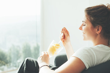 Happy young woman sitting near big bright window eating ice cream