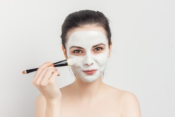 white mask on the face of a beautiful brunette and makeup brush