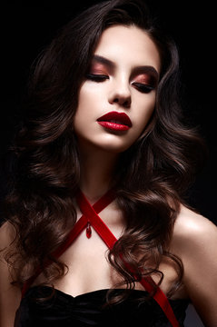 Young girl with a black lace mask on her face and a pendant in the form of heart on the neck. Beautiful model with bright make-up, red lips and curls. The picture on Valentine's Day.