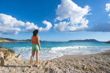 Woman in an orange T-shirt and shorts looking into the distance on the seashore