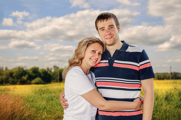 Young man and woman, woman standing and hugging in a field