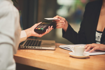 Mixed race woman in coffee shop using credit card and smart watch for paying. NFC paying concept.