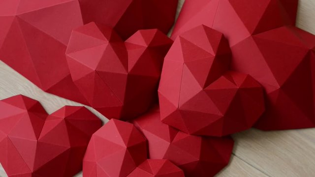 Heap of red polygonal paper heart shapes on wooden background, top view, rotating video