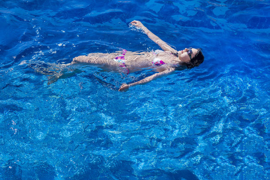 Woman in bikini and sunglasses  swims in the pool