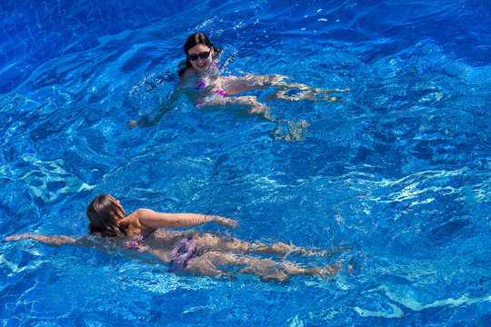  Two women in bikini swims in the pool