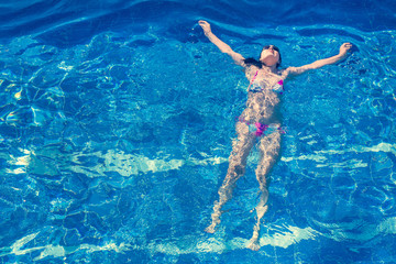 Woman in bikini and sunglasses  swims in the pool