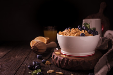 Healthy breakfast with corn flakes, berries and milk on old dark wooden background. Copy space. Retro style toned.