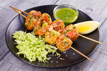 Cilantro grilled shrimps on skewers with sesame napa cabbage, green butter sauce and lemon. Skewered prawns on black plate