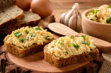 Whole wheat sandwiches with egg and cheese spread on wooden stump.