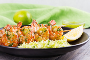 Cilantro grilled shrimps on skewers with sesame napa cabbage, green butter sauce and lemon. Skewered prawns on black plate