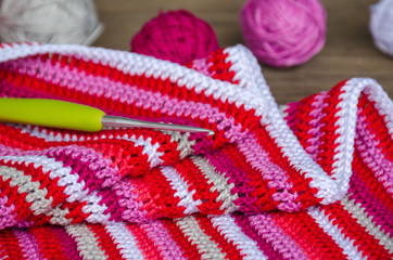 crocheted striped fabric in red colors with crochet hook and many small yarn balls on the old wood...
