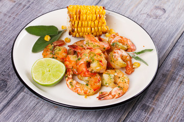 Grilled shrimps and corn garnished with lime and sage leaves. Prawns on white plate