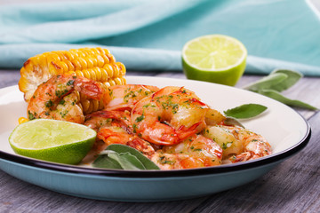 Grilled shrimps and corn garnished with lime and sage leaves. Prawns on white plate