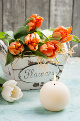 orange tulips in wooden basket and lit cadle