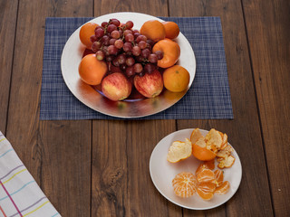 Plates with fruits on a wooden table, grapes, apples, clementines, orange. peeled clementines.