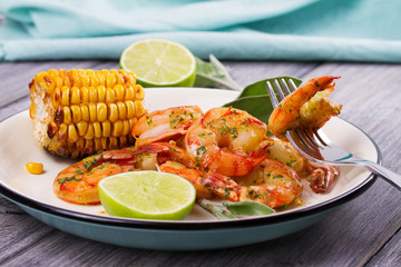 Grilled shrimps and corn garnished with lime and sage leaves. Prawns on white plate