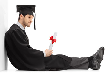 Sad graduate student with a diploma sitting on the floor