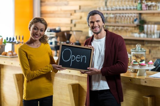 Smiling owners standing with open sign board in cafe