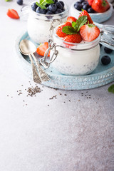 Chia Pudding for breakfast in glass jars garnished with berry in two portions on light gray stone background with a napkin and spoons. Copy space.