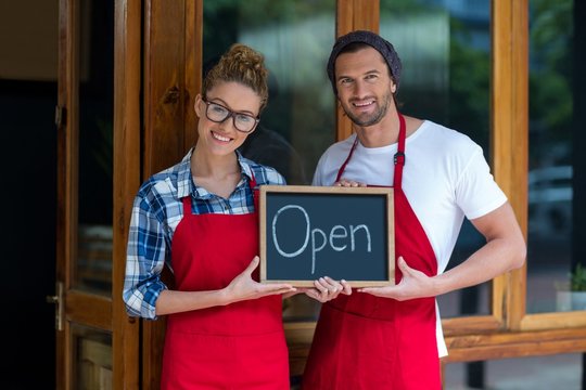 waitress and waiter standing with open sign board 