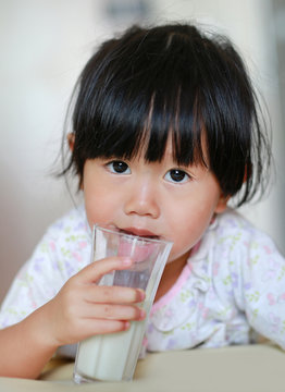Close up of little girl in pajamas drinking milk from glass indoor at the morning.