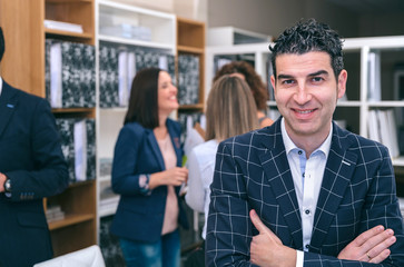 Portrait of smiling curly businessman looking at camera in the office with colleagues talking on background