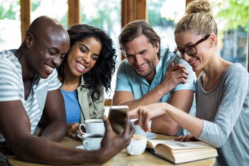 Obraz premium Group of friends using mobile while having cup of coffee