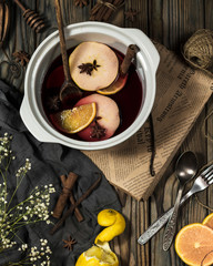 Mulled wine in making with oranges, apples, spices, spoon, fork, flowers on a wooden table slightly...