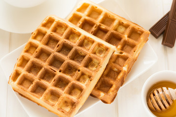 Traditional breakfast: coffee, belgian waffles with honey and chocolate sauce on white wooden table. Selective focus