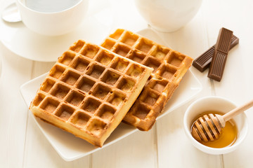 Traditional breakfast: coffee, belgian waffles with honey and chocolate sauce on white wooden table. Selective focus