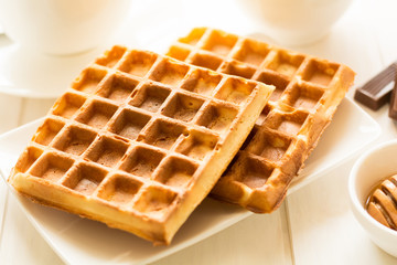 Traditional breakfast: coffee, belgian waffles with honey and chocolate sauce on white wooden table. Selective focus