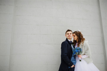 Young wedding couple at cold winter day against white stone wall