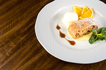 Apple strudel with ice cream and orange on white plate